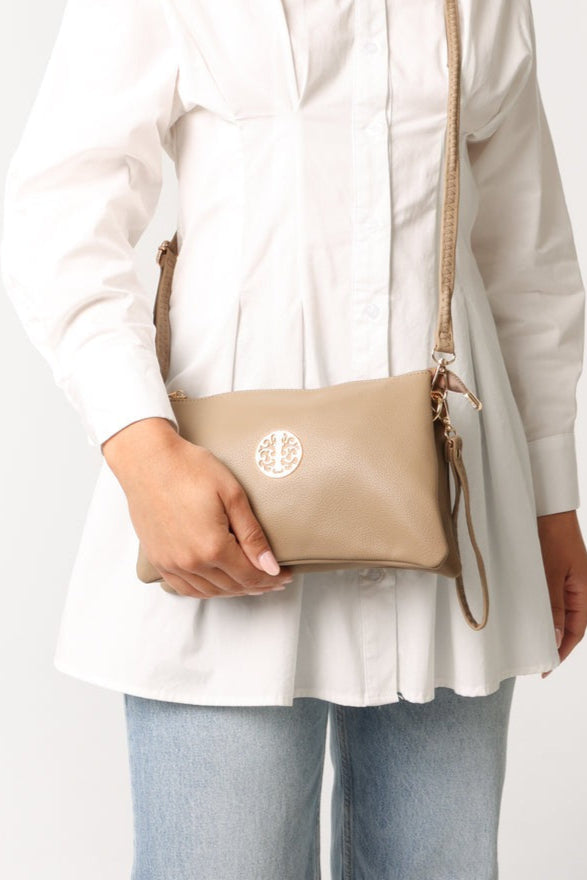 Person holding a beige handbag with a visible brand logo against a white background