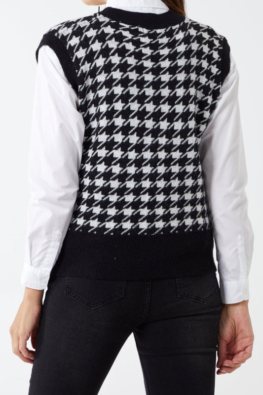 Person wearing a black and white houndstooth patterned sweater over a white shirt with a plain background