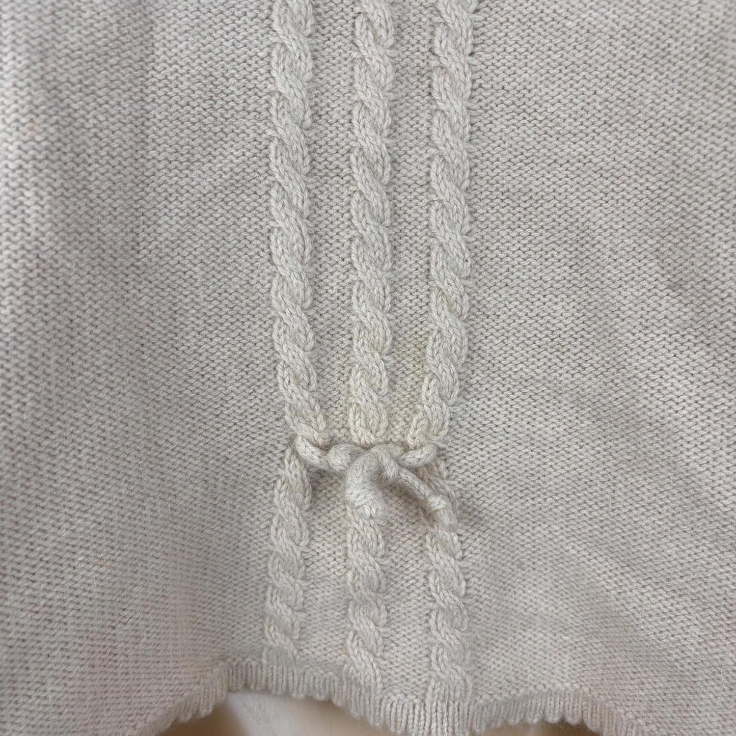 Close-up of a light pink knitted garment with a braided trim.