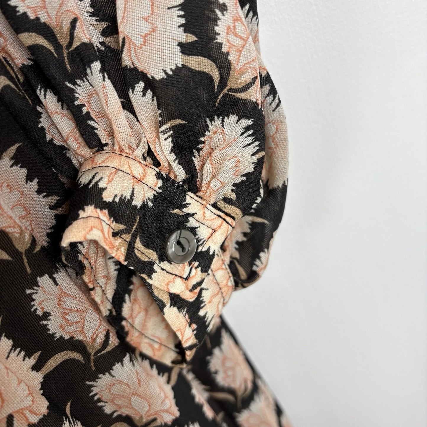 Close-up of a floral patterned shirt with black, beige, and white colors on a plain background.