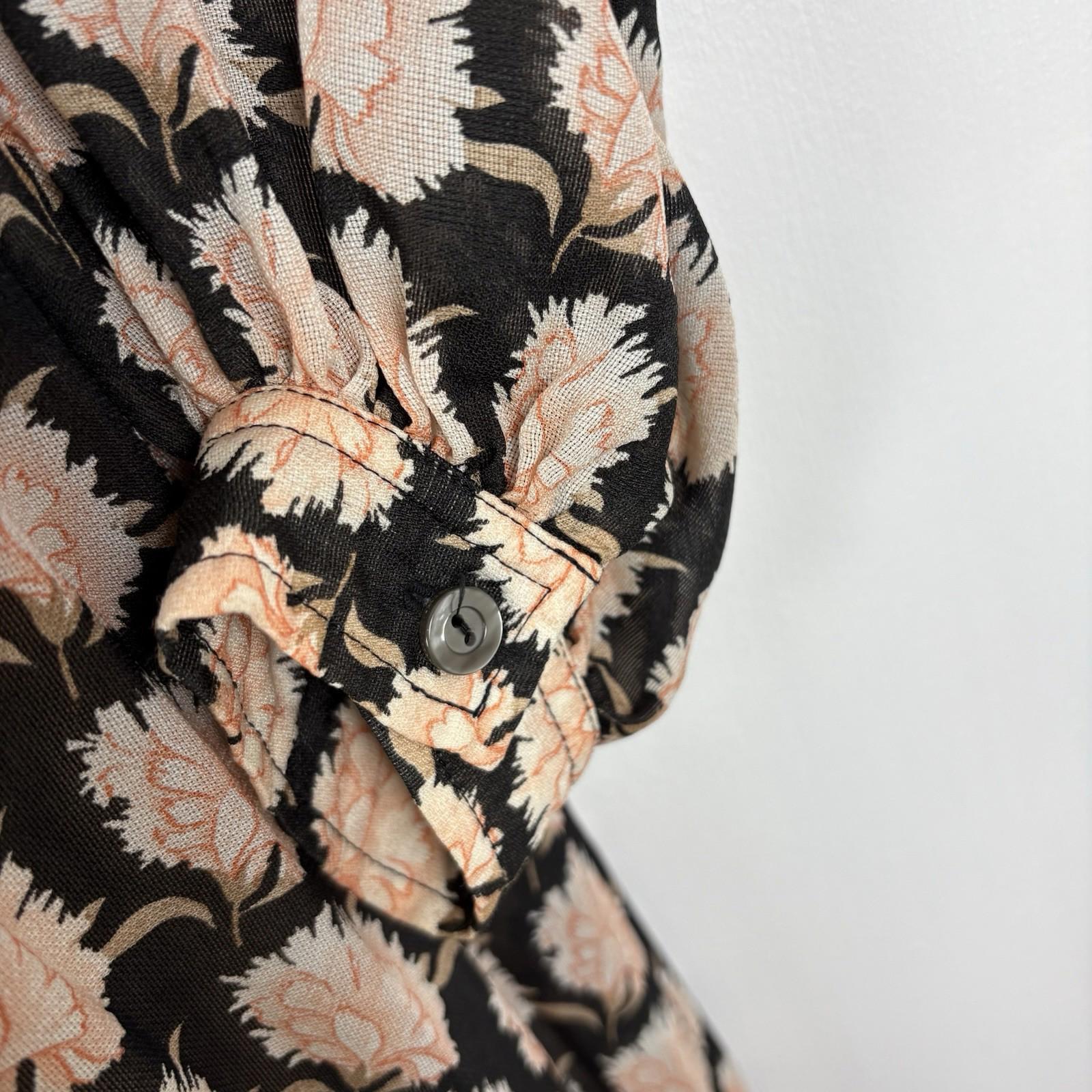 Close-up of a floral patterned shirt with black, beige, and white colors on a plain background.