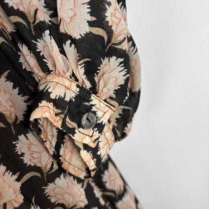 Close-up of a floral patterned shirt with black, beige, and white colors on a plain background.