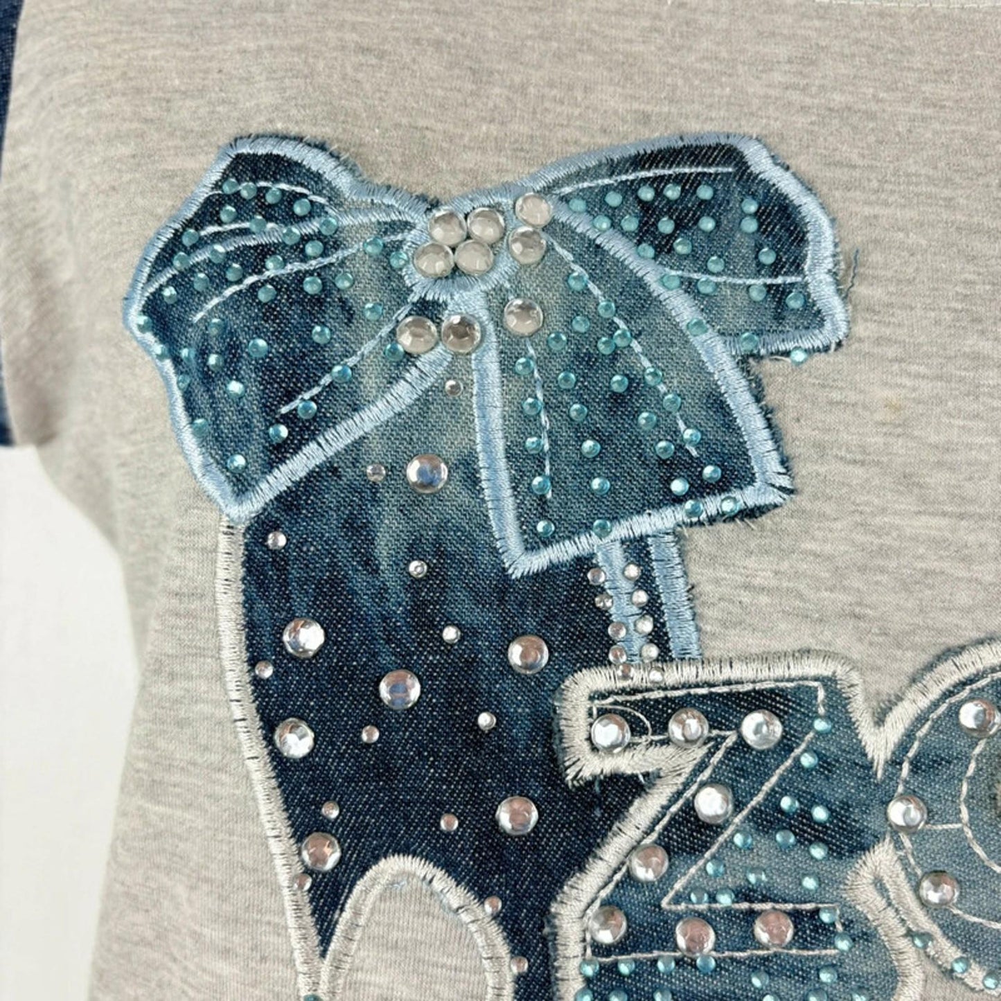 Embroidered design of a dog with a bow on a gray background