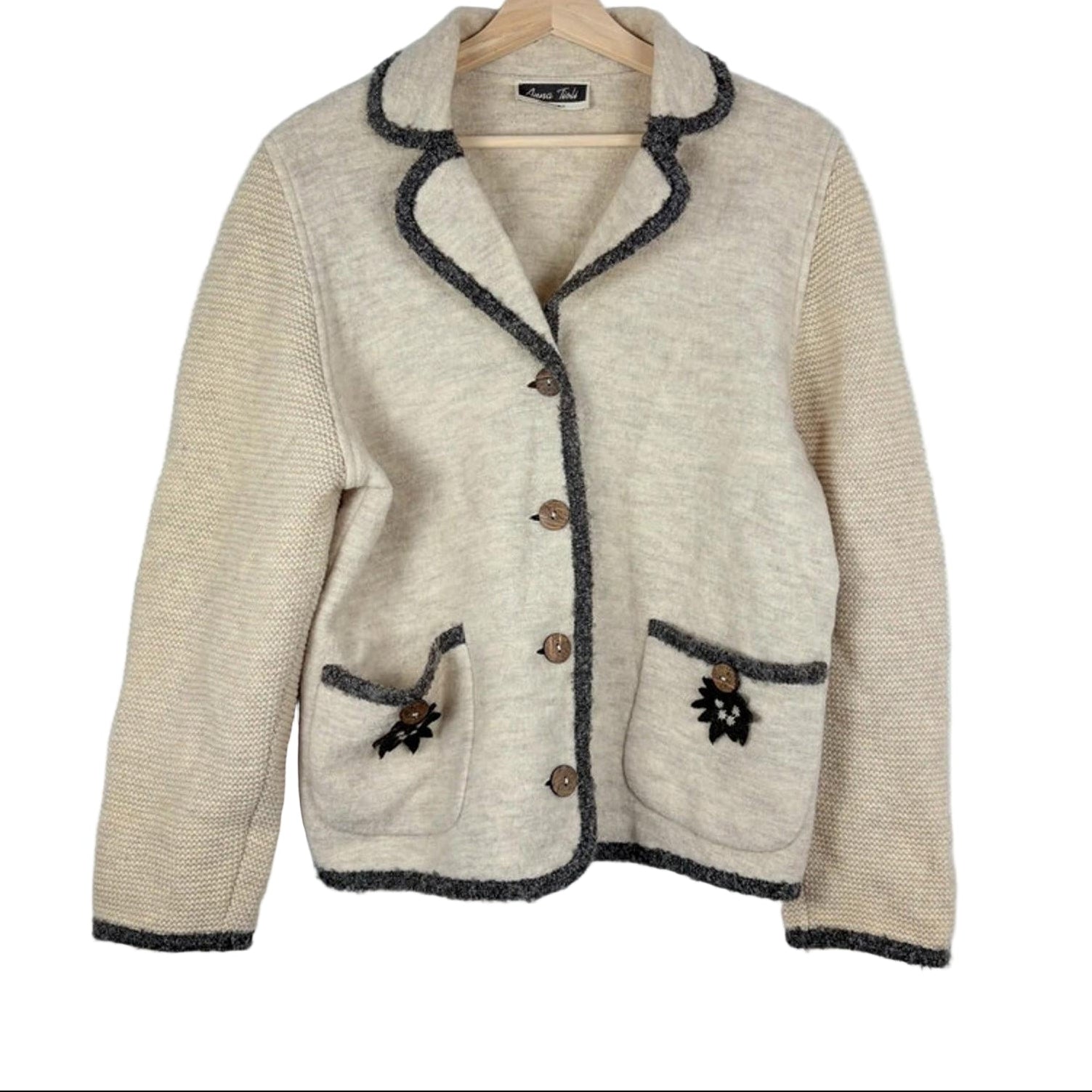 Beige jacket with dark trim on a hanger against a white background