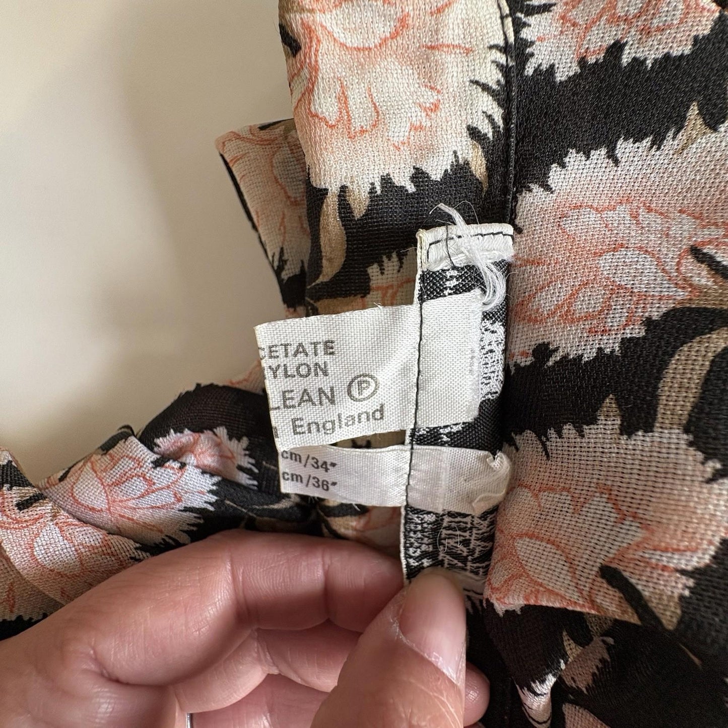 Floral-patterned fabric with a label held by a hand against a neutral background