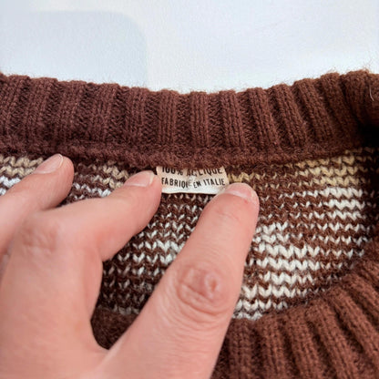 Close-up of a hand holding a brown knitted fabric with a visible label.