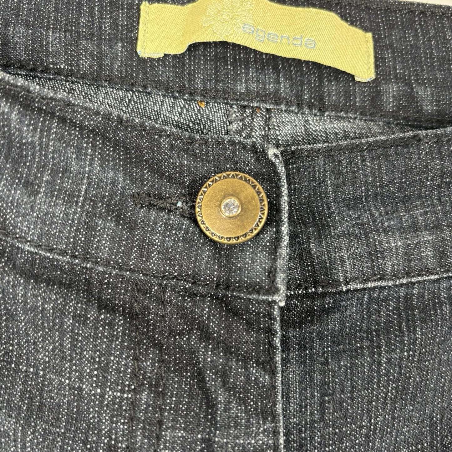 Close-up of a button on black denim jeans with a brand label.