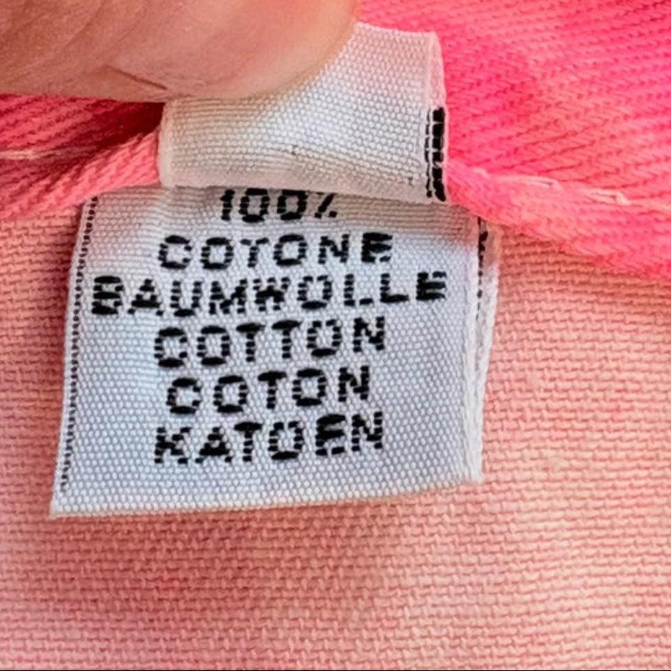 Close-up of a hand holding a pink fabric with a label indicating 100% cotton.
