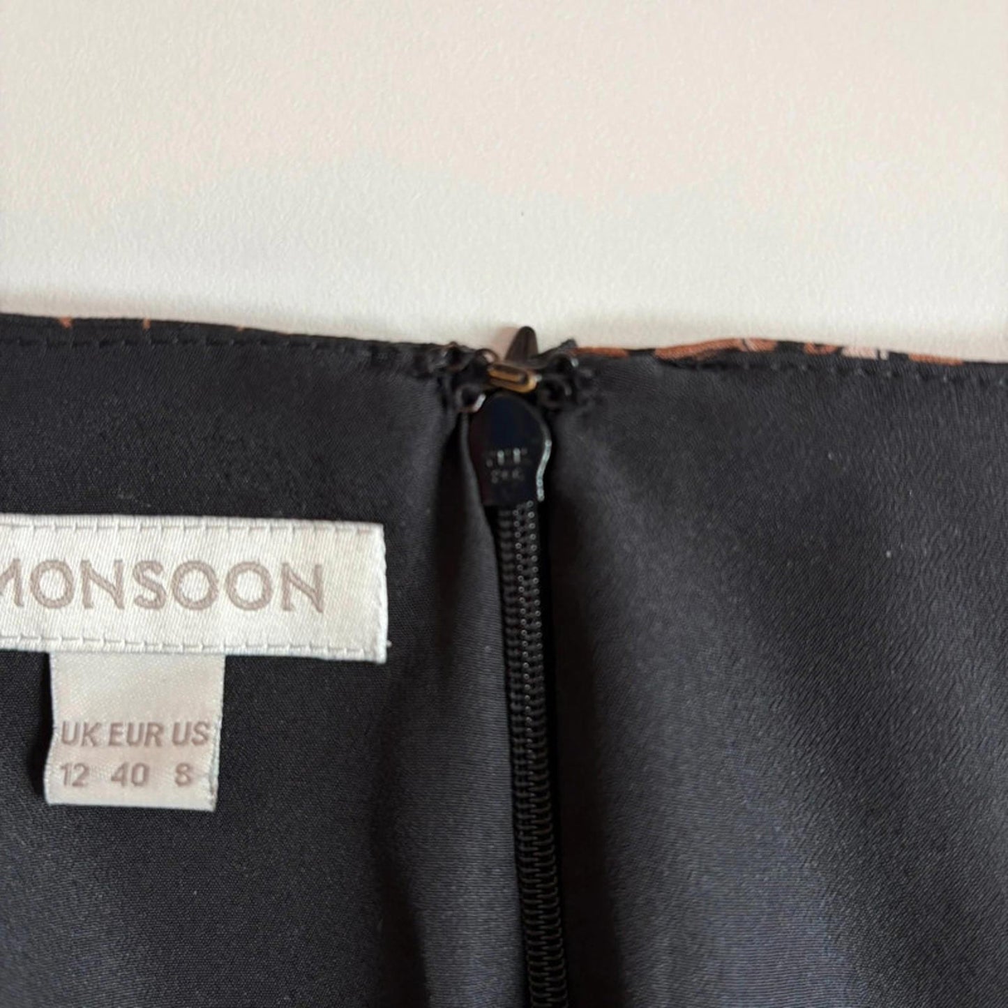 Close-up of a Monsoon label on a garment with a zipper.