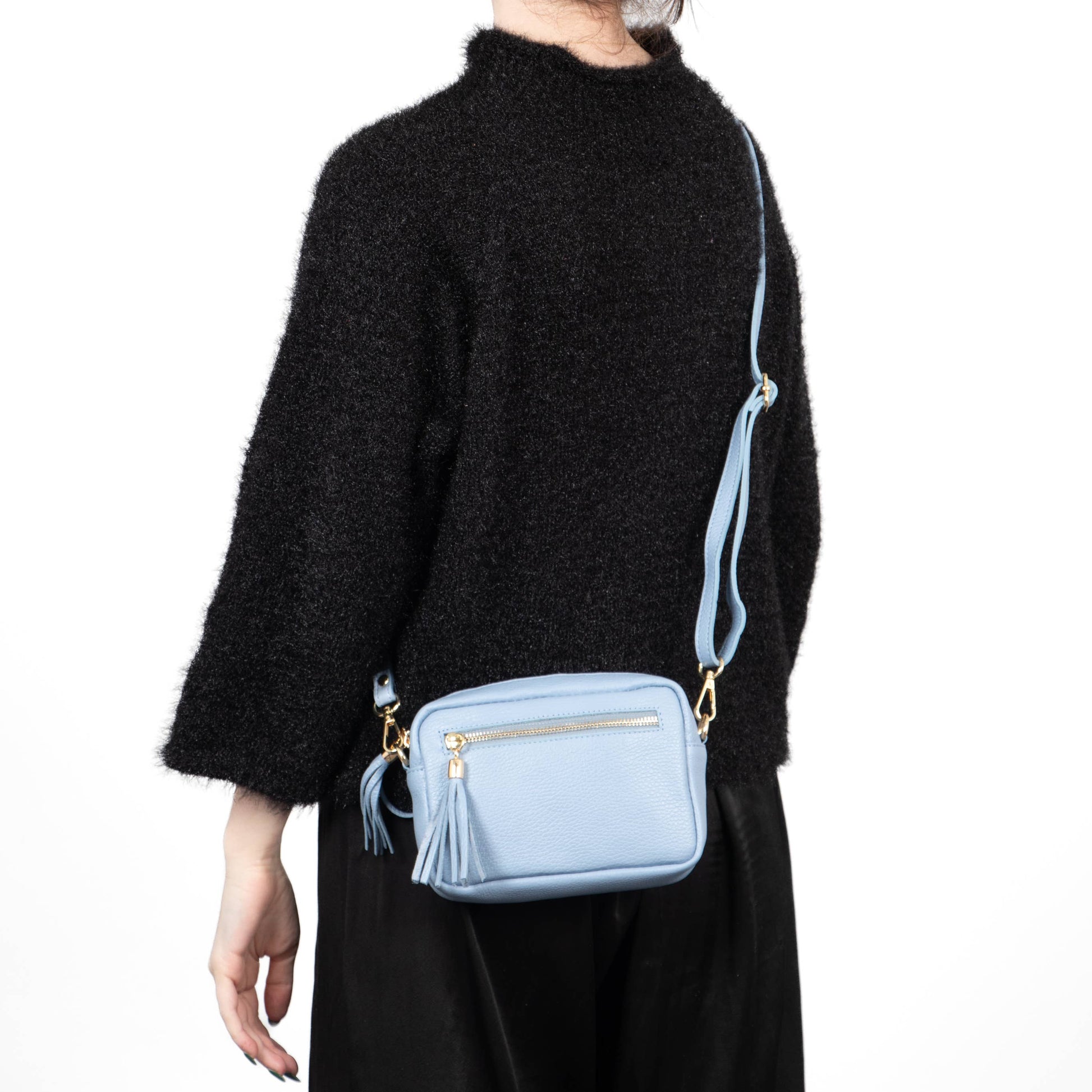 Person wearing a black sweater and holding a light blue handbag with a strap.