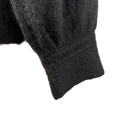Close-up of a black knitted sweater sleeve on a mannequin arm.