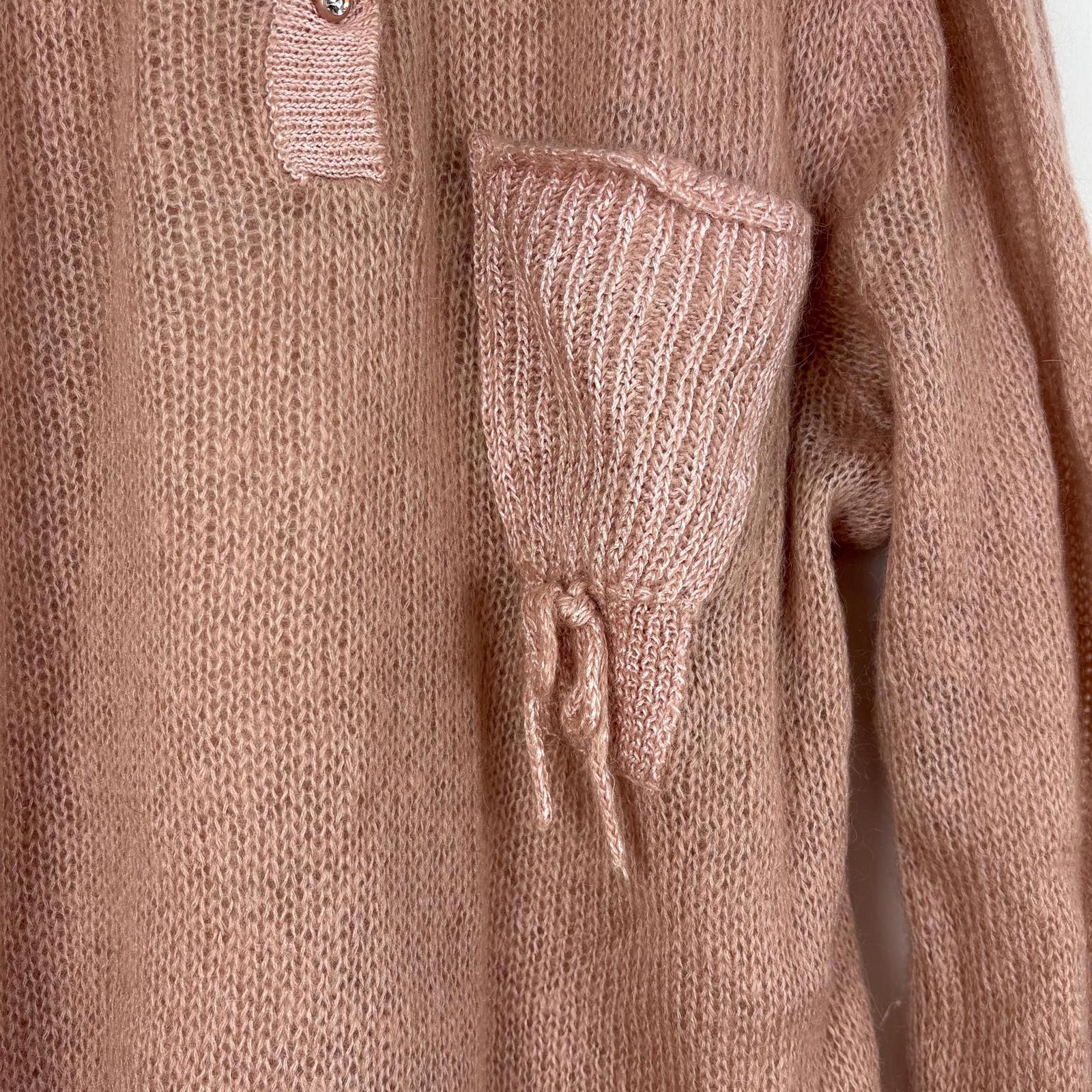 Close-up of a pink knitted sweater with a drawstring pocket detail.