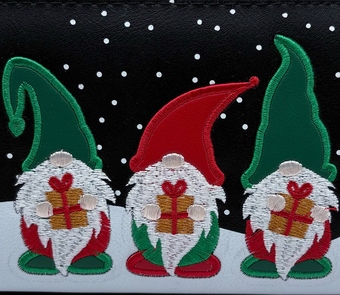 Three embroidered gnomes with red hats and gift boxes on a black background with white dots.