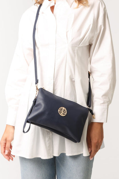 Person wearing a navy handbag with a gold emblem on a plain background