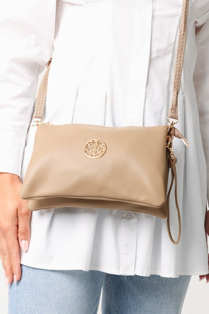 Beige crossbody bag with a brand logo worn by a person in a white shirt and light blue jeans.
