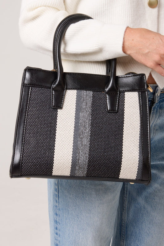 Black and white striped handbag held by a person wearing a white sweater and blue jeans.