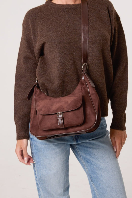 Person wearing a brown suede bag over one shoulder against a plain background