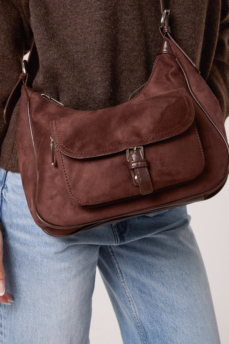 Brown leather handbag worn over the shoulder with a neutral background