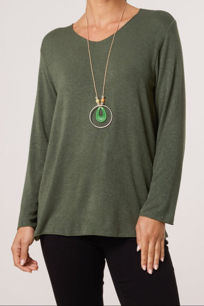 Person wearing a green long-sleeve top and black pants with a gold necklace featuring a green pendant on a white background.