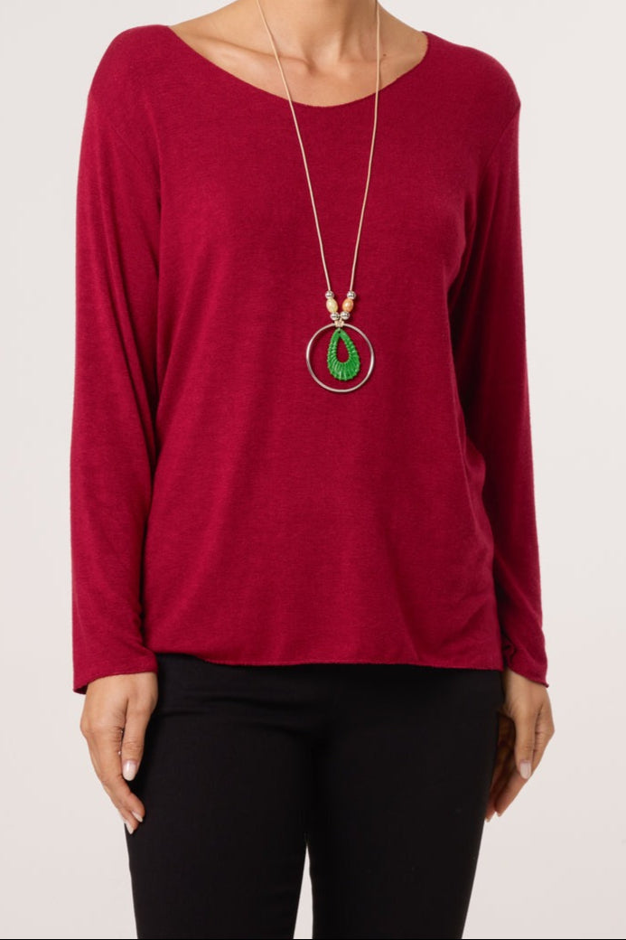 Red long-sleeve top worn by a person with a necklace featuring green and red elements on a white background