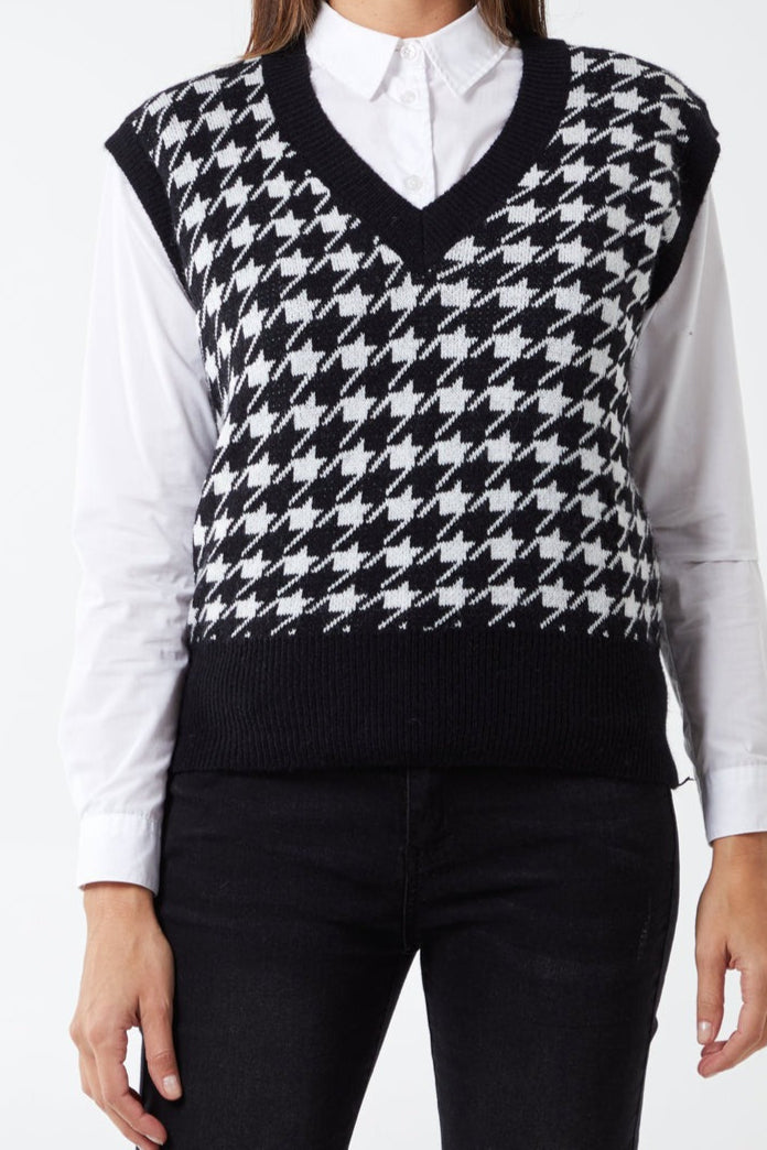 Person wearing a black and white houndstooth patterned sweater vest over a white shirt.