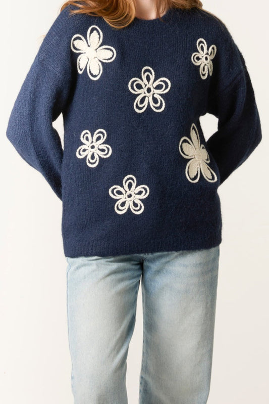 Navy sweater with white floral patterns worn by a person on a plain background