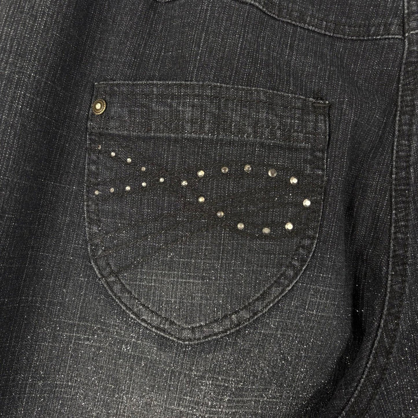 Close-up of a dark denim shirt with a pocket featuring decorative studs.