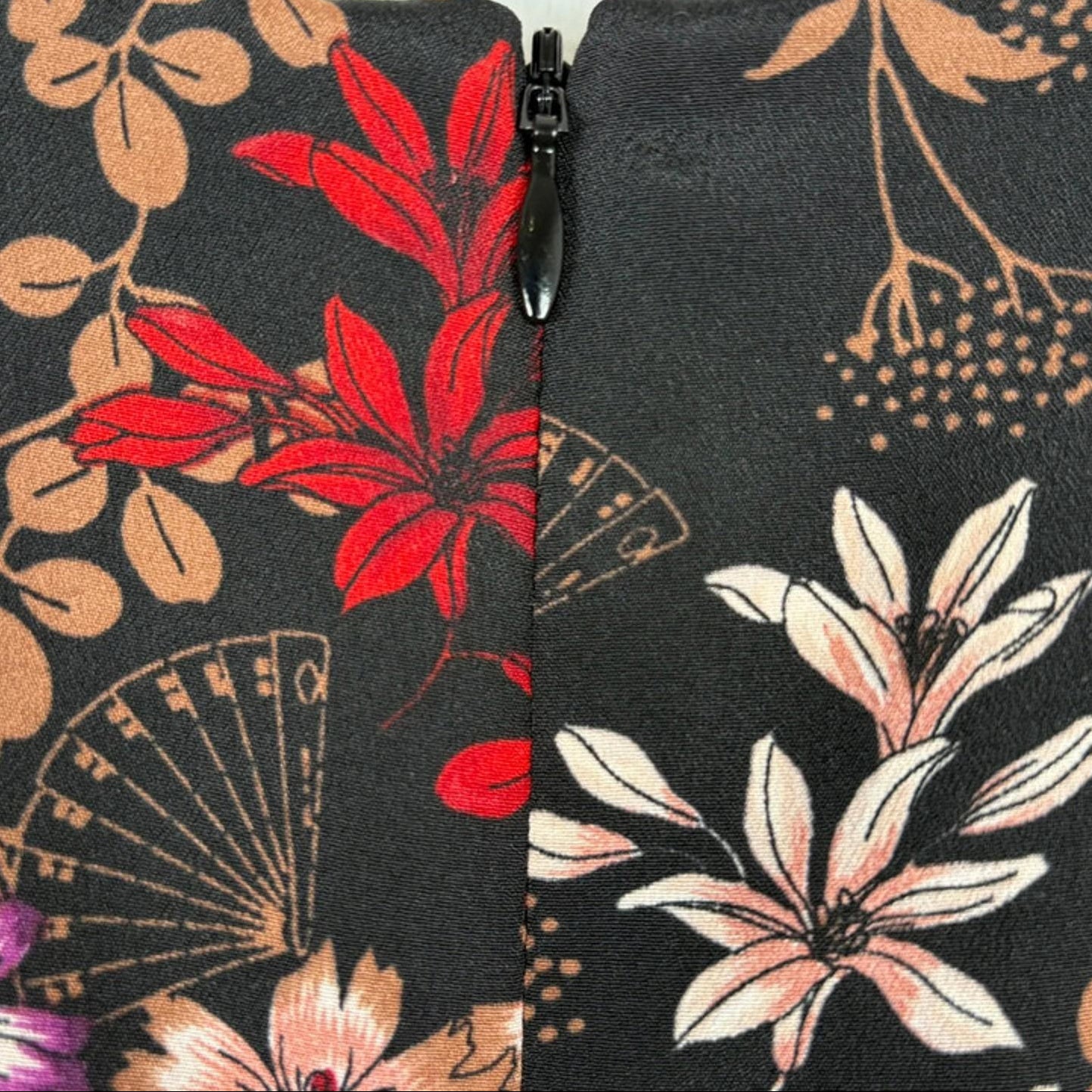 Close-up of floral-patterned fabric with a zipper, featuring red, pink, and beige flowers on a black background.