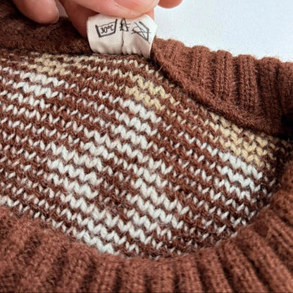 Close-up of a brown and white striped sweater with a hand holding a label.