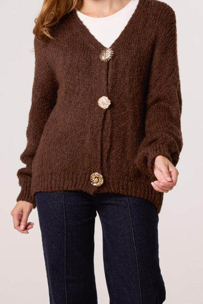 Brown cardigan with gold buttons worn by a person on a white background